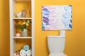 Shelves with different stuff above toilet bowl near orange wall