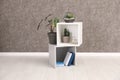 Shelving unit with indoor plants and books for interior design on floor at grey wall. Trendy decor Royalty Free Stock Photo