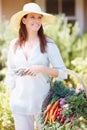 Shes an avid gardener. A beautiful woman standing in her garden while holding a basket of vegetables.