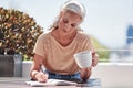 Shes an avid writer. an attractive senior woman enjoying a cup of coffee while writing in her book outside on the
