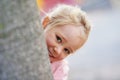 Shes got a mischievous look in her eyes. Portrait of a cute little girl peeking out from behind a tree.