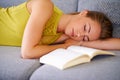 Shes got a relaxed weekend ahead of her. a young woman sleeping beside a book on her sofa at home. Royalty Free Stock Photo