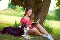 Shes in her happy place. a young woman reading a book while sitting with her dog under a tree.