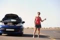 Shes in need of some road side assistance. A beautiful young woman standing with her broken-down car hitching a ride on Royalty Free Stock Photo