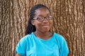 Shes not a tree hugger but she sure loves em. Portrait of a pretty black teen smiling while standing against a tree. Royalty Free Stock Photo