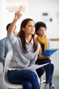 Shes outspoken in the work place. A beautiful young woman sitting with her hand raised to ask a question.