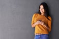 Shes a social butterfly. An attractive young woman holding up a mobile phone while standing against a gray wall. Royalty Free Stock Photo