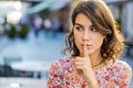 Young woman presses finger to lips makes silence hush sign do not tells gossip secret quiet in city Royalty Free Stock Photo