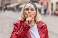 Senior woman presses finger to lips makes silence hush sign do not tells gossip secret quiet in city Royalty Free Stock Photo