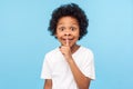 Shh, be quiet! Portrait of funny cute little boy with curly hair in T-shirt making silence gesture with finger on his lips