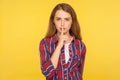 Shh, be quiet! Portrait of serious ginger girl in checkered shirt holding finger on lips making hush silence gesture