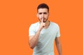 Shh, make silence please! Portrait of serious brunette man showing quiet gesture. isolated on orange background