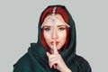 Shh. Pretty woman showing shh, hush, silence gesture with hand on light gray grey background green hijab scarf and tikka oriental Royalty Free Stock Photo