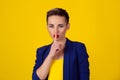 SHH. Woman wide eyed asking for silence or secrecy with finger on lips hush hand gesture yellow background wall. Pretty girl Royalty Free Stock Photo