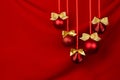 Shimmer red balls with gold bows hang on ribbons in row on deep scarlet silky smooth wavy wall, closeup, copy space. Luxury New. Royalty Free Stock Photo