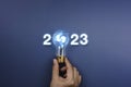 Shining 2023 calendar year numbers, neon style with creative trend light bulb holding by businessman`s hand.