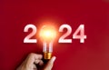 Shining 2024 calendar year numbers, neon style with creative trend light bulb holding by businessman's hand.