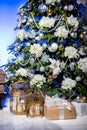 Shining Christmas tree decorated with balls and flowers, gifts and candles in cages under it in living room. Christmas evening. Royalty Free Stock Photo