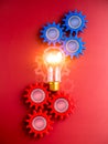 Shining light bulb connected between blue and red gear wheels on red background, vertical style. Royalty Free Stock Photo