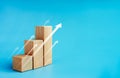 Shining rise up arrow on wooden cube blocks, bar graph chart steps on blue background.