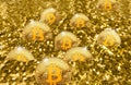 Shiny Bitcoins cryptocurrency pieces are almost buried in a large pile of shiny gold