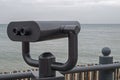 Shiny black binoculars on a swivel hinge on observation deck on sea embankment, directed to the right at horizon with azure sea