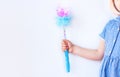 Shiny blue magic wand in the hand of a girl in plaid dress on light background faceless with copy space. Happy birthday