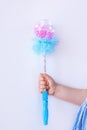 Shiny blue magic wand in the hand of a girl in plaid dress on light background faceless with copy space. Happy birthday
