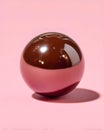 Shiny chocolate sphere on pastel pink background casting soft shadow in minimalistic composition, close-up Royalty Free Stock Photo