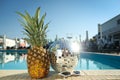 Shiny disco ball, pineapple and sunglasses on edge of swimming pool. Party items