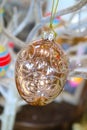 Shiny glittery golden Eastern ornament hangs by a gold cord from white branches with other colorful egg ornaments blurred behind