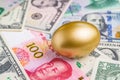 Shiny golden egg on pile of Chinese Yuan and US America dollar banknotes money metaphor of finding the good stock with high Royalty Free Stock Photo