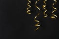 Shiny golden serpentine streamers on black background, flat lay. Space for text