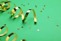 Shiny golden serpentine streamers and confetti on green background, closeup