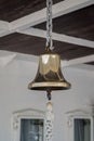 Shiny goldish ship bell hanging on chain with tongue ending in hook with attached braided rope. Bulkheads of  lower upper deck. Royalty Free Stock Photo