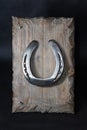 A shiny metal horseshoe, nailed to an old board with forged key holder nails