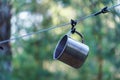 A shiny metal mug is hanging on a hook in the woods by a tree. A rope is stretched between the trees around the tent camp. Tourist Royalty Free Stock Photo