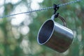 A shiny metal mug is hanging on a hook in the woods by a tree. A rope is stretched between the trees around the tent camp. Tourist Royalty Free Stock Photo