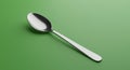 A shiny metal spoon is placed diagonally on a smooth, solid green background. The Royalty Free Stock Photo