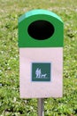Shiny metal trash can with mounted box and large opening for garbage and dog waste surrounded with uncut grass in local public