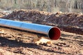 Shiny new large diameter pipe at local oil pipeline construction site supported with wooden supports on top of wet soil Royalty Free Stock Photo