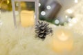 Shiny pine cone on white fluffy carpet with unfocused white candle on foreground and bokeh lights on background. Merry Christmas Royalty Free Stock Photo