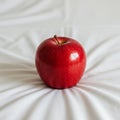 A shiny red apple is placed centrally on a white, slightly wrinkled fabric surface. The Royalty Free Stock Photo