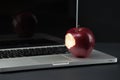 Shiny red apple resting on an open aluminum laptop in selective focus on a black background Royalty Free Stock Photo