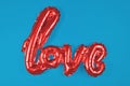 Shiny red balloon forming the word `love` on bright blue background