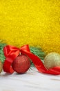 Shiny red and gold balls with bow and twisted ribbon at back of spruce branch. Yellow blurred glitter vertical background Royalty Free Stock Photo