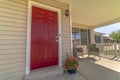 Shiny red wooden front door of a home with wicker chairs on the sunlit porch Royalty Free Stock Photo