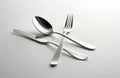 Shiny silver cutlery set includes spoon, knife, and fork arranged on a clean white surface. Simple elegant composition for Royalty Free Stock Photo