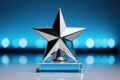 Shiny silver star trophy on clear glass base blue bokeh background Royalty Free Stock Photo