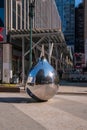 Shiny stainless steel tear drop shaped sculpture seen on a street in Manhattan New York. There is a reflection of a large building